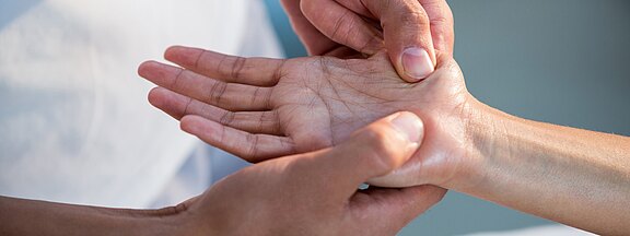 Nahaufnahme: Eine Person hält die geöffnete Hand einer anderen und drückt mit dem Daumen auf den Handballen – Handmassage, Akupressur oder Untersuchung.